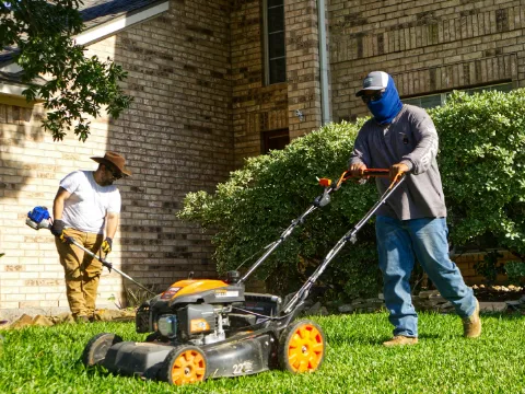 A two-person crew mowing and trimming a front lawn.